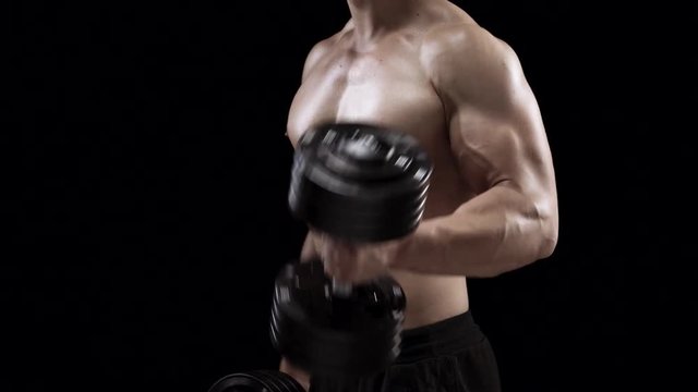 Man flexes his hands with dumbbells, training his biceps on a black background in the studio, side view