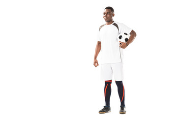 Fototapeta na wymiar full length view of smiling young african american soccer player holding ball and looking away isolated on white