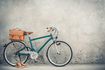 Retro bike with aged leather postman's bag and old sneakers front concrete wall background. Vintage...