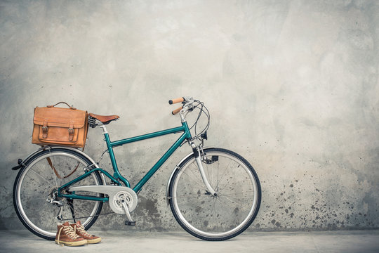 Fototapeta Retro bike with aged leather postman's bag and old sneakers front concrete wall background. Vintage style filtered photo