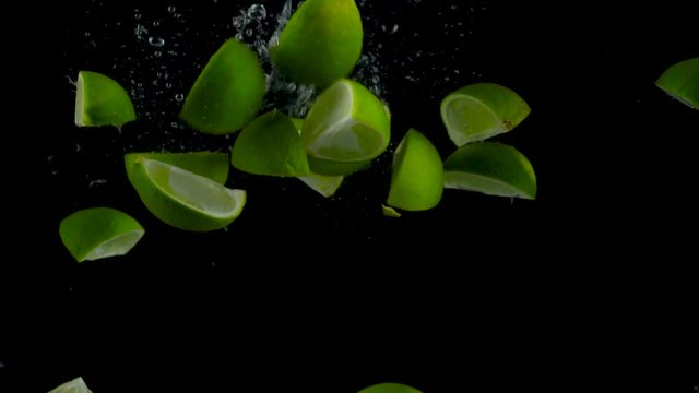 Lime pieces fall and float in water, black background, slow motion