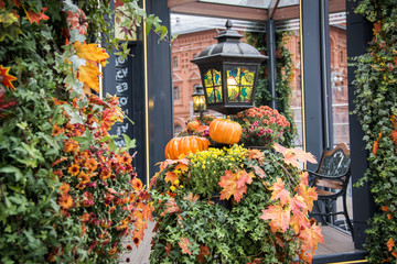 Autumn outdoor decorations. Orange pumpkin and retro forged lanterns with maple leaves,flowers and hawthorn berries in a pavillion. Red brick building