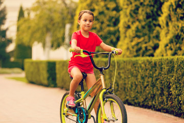 Fototapeta na wymiar Child riding bike. Kid on bicycle in sunny park. Little girl enjoying bike ride her way to school warm summer day. Preschooler learning to balance bicycle Sport for kids.