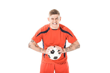 angry young soccer player holding ball and looking at camera isolated on white