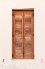 Old wooden window with brown shutters on weathered wall.