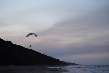 Seascape with silhouettes of the mountains and coast of sea at sunset. Paraglider flying over the beach