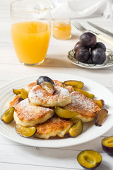 Cheese pancakes in powdered sugar with fresh plums on a plate