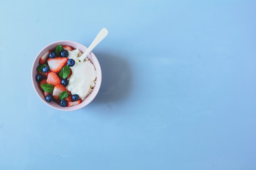 Bowl with cottage cheese, cream, strawberry, blueberry and mint leaves on blue background. Top view. Toned