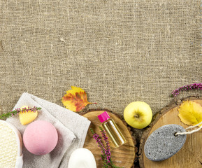 Fototapeta na wymiar Cozy autumn setting with spa essentials for nice relaxing evening. On burlap cloth background are soap bar, massage oil, bath bomb, towel, pumice stone. Bottom border a lot of copy space.