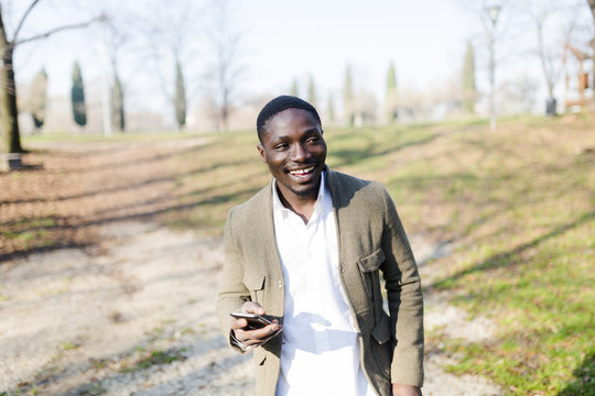 Portrait of young man in park, wearing jacket, holding smartphone