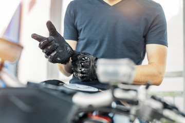 Close up of biker putting on black gloves and sitting on motorcycle.