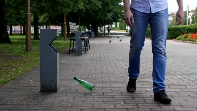 A young man throws a plastic bottle in the city near a trash can