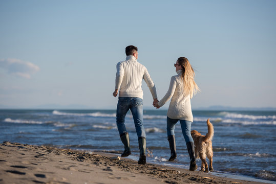 couple with dog having fun on beach on autmun day