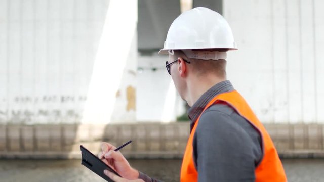 A man inspector examines the condition of the columns of the bridge across the river and marks the shortcomings, engineering, close-up
