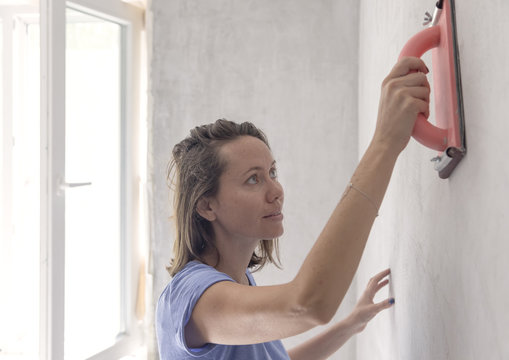 Young woman working with rubbing board on plaster