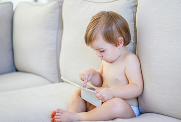 Cute little baby playing digital tablet sitting on the sofa. Parenting control. Child internet safety concept.