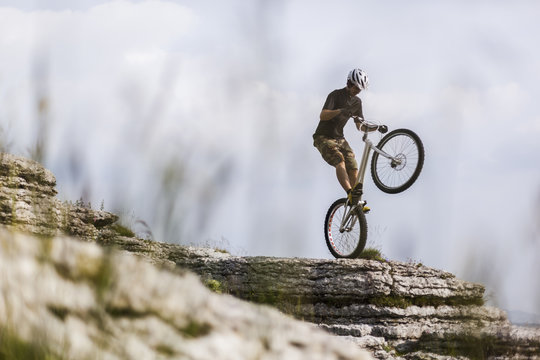 Acrobatic biker performing stunt over rock against sky