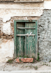 Blocked old green wooden door with cracks, on weathered wall.