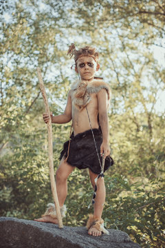 Caveman, manly boy with staff and bow hunting. Prehistoric tribal boy outdoors on nature. Young shaggy and dirty savage, warrior and hunter. Primitive ice age man in animal skin standing against