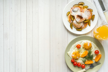 Concept of Breakfast. Fried eggs, cottage cheese pancakes, plums and oatmeal with milk, orange juice on the table