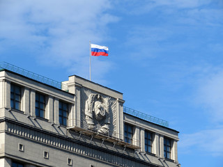 Russian flag on Parliament building in Moscow against blue sky. The State Duma facade with old...