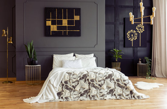 White pillows on patterned bed in grey bedroom interior with black and gold posters. Real photo