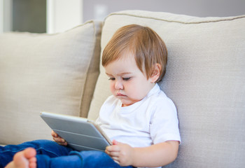 Cute little baby watching cartoon on digital tablet sitting on the sofa. Parenting control. Child...