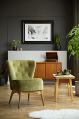 Real photo of green chair standing in grey living room interior with poster and molding on wall,...