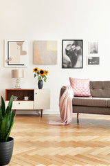 Gallery in white living room interior with sofa with pink pillow and coverlet, sunflowers on...