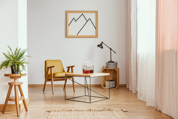 Plant on wooden stool in white living room interior with poster and yellow armchair. Real photo