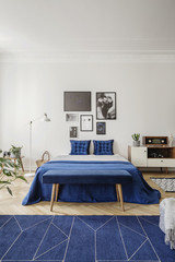 Navy blue bed and radio on cabinet in white bedroom interior with posters and carpet. Real photo