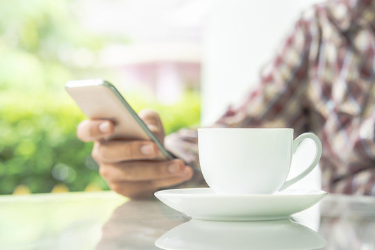 Male hands holding smart phone and cup of coffee on the table