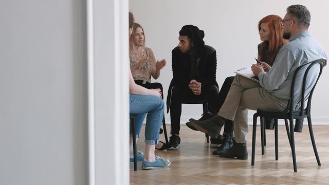 Teenagers and psychotherapist listening to young woman while sitting in the circle during therapy