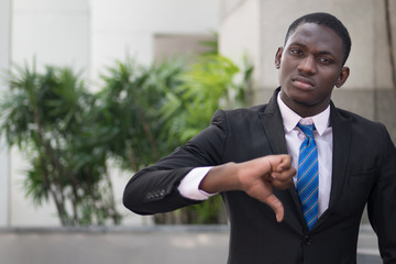 african businessman giving thumb down; portrait of upset angry african business man showing failed thumb down gesture for loser, profit lost, failed business deal; young adult african man model
