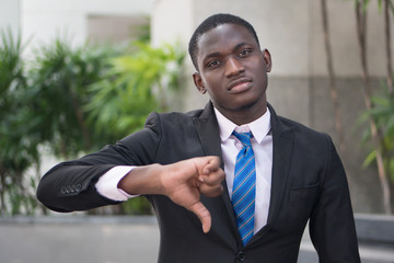 african businessman giving thumb down; portrait of upset angry african business man showing failed thumb down gesture for loser, profit lost, failed business deal; young adult african man model