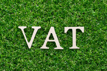 Wood alphabet in word VAT (Abberviation of Value added tax) on artificial green grass background