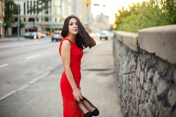 Beautiful Girl in a red dress is standing near of the roadway.