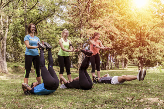 three couples sporting their exercises outdoor together. sportsmen push up their legs to train abdominal muscles similar to situps.