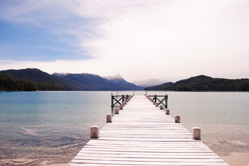 Patagonian wooden pier / In a lake, with mountains in the horizon and the sun hidden behind a soft cloudy sky / Villa la Angostura, Patagonia Argentina