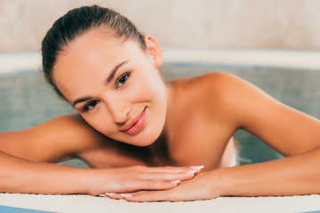 woman relaxing in swimming pool in spa salon and looking at camera