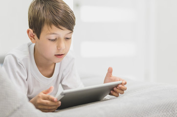 Active little boy sitting on sofa watching tablet , Happy kid boy relaxing on sofa on a bright sunny say, Child with technology concept