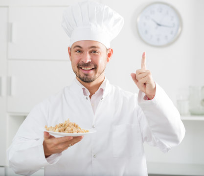 Young happy european cook in cap offering oat porridge for breakfast