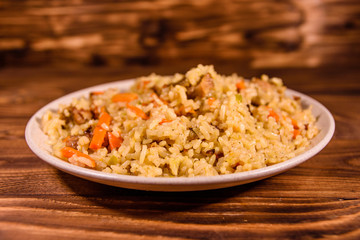 Ceramic plate with pilaf on wooden table