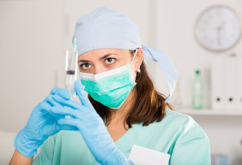 Female nurse in mask holding syringe for injection in hospital