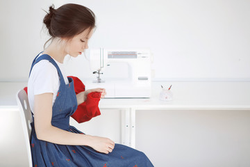 Happy attractive young woman seamstress sitting and sews on her arms near sewing machine in studio