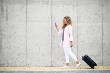 Woman carrying luggage and using smart phone while walking to the station.