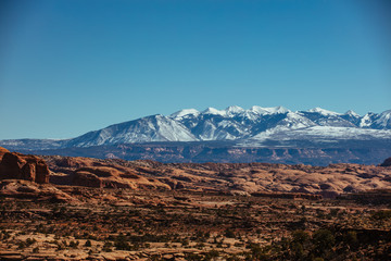 Snow Capped Peaks Over The Red Rock Desert Landscape Of Utah In The Iconic American Southwest