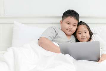 Brother and sister play laptop on bed together