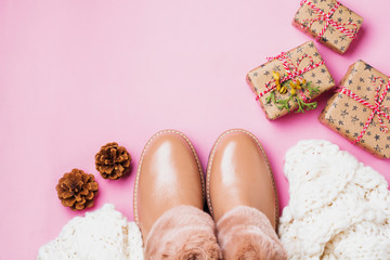 Leather women's warm shoes with fur, white scarf and gifts boxes on light pink background. Сoncept of the New Year season. Top view. Cope space.