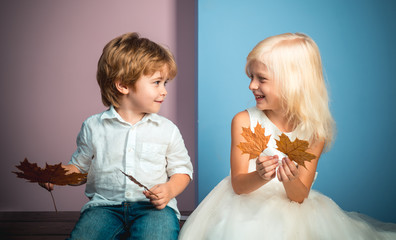Cute little boy and girl holding leaf on color background. Funny face and happy baby. Children advertise your product and services. Autumn discounts on baby clothes.
